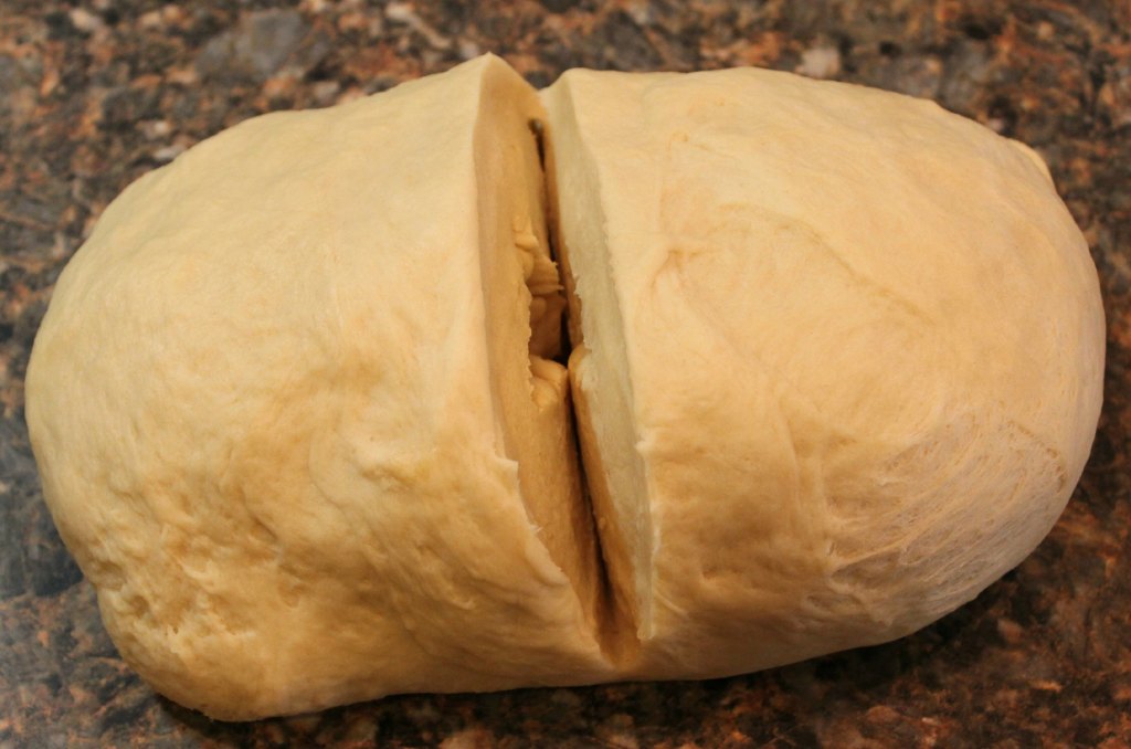 A chunk of bread dough divided in half on the counter.