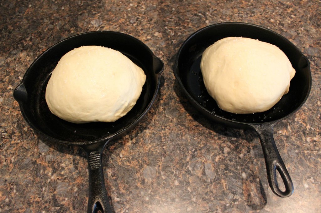 Two cast iron skillets with bread dough rising in them.
