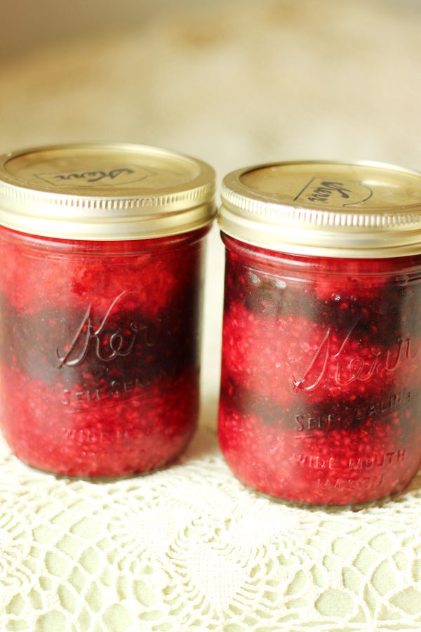 Two jars of no cook berry jam.  The jam has been layered into the jar in stripes so you can see a layer of raspberry, layer of blackberry, and layer of strawberry.