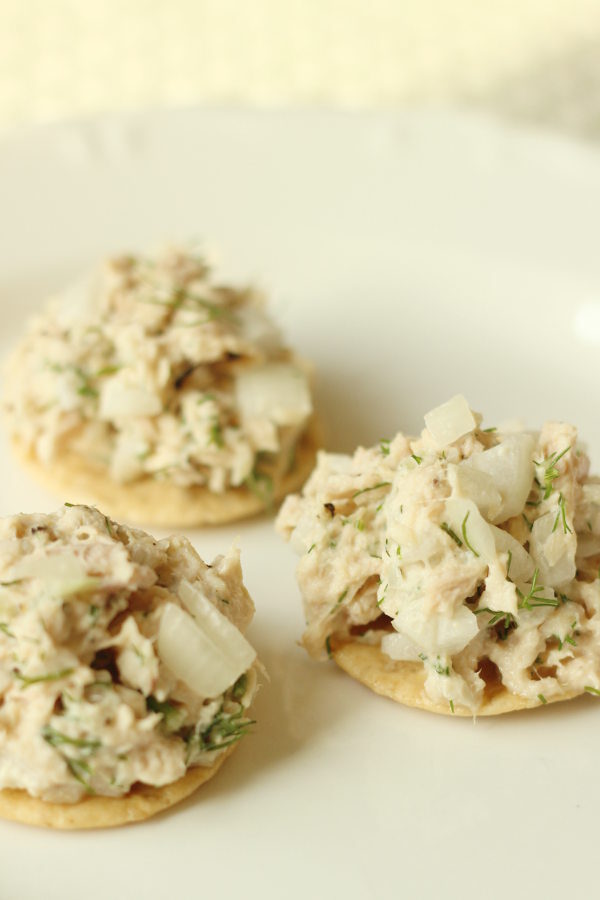 Three rice crackers are loaded up with mounds of healthy tuna salad. You can see fresh dill and small pieces of onion.
