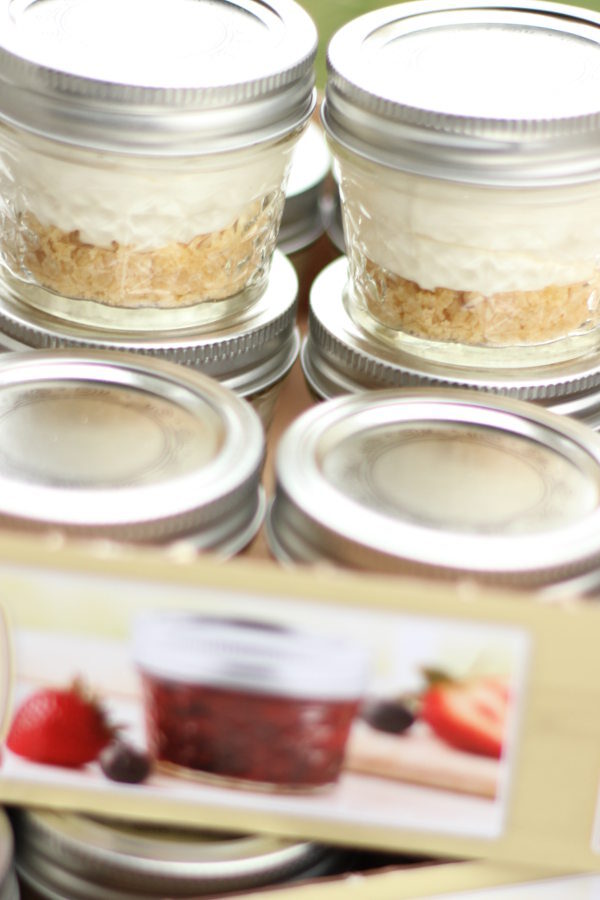 Small fruit tarts are made in 4oz mason jars. You can see the layer of shortbread cookie crust, creamy filling, and then the lids on top so they can be stacked for stoarage.