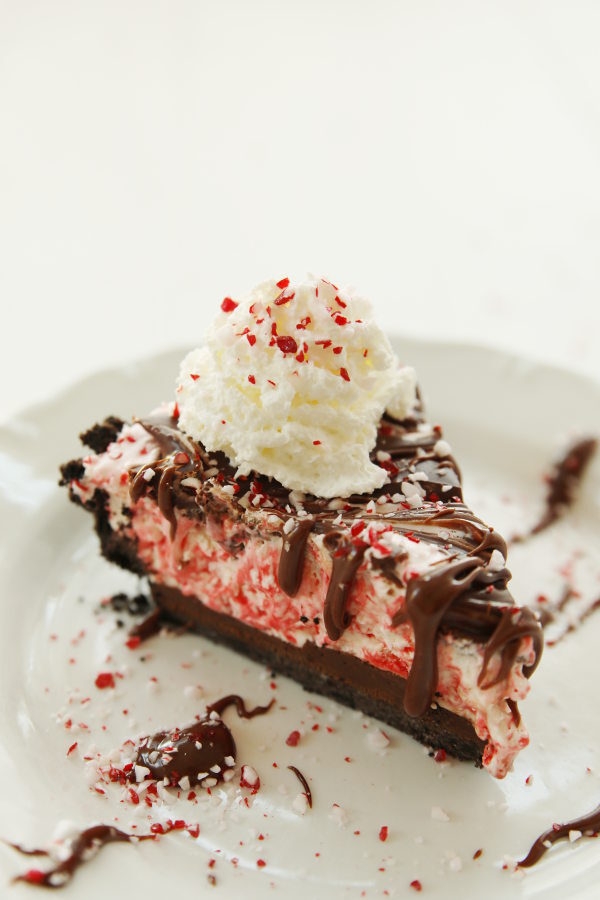 A big slice of candy cane pie sits on a white plate with some candy cane pieces scattered around.