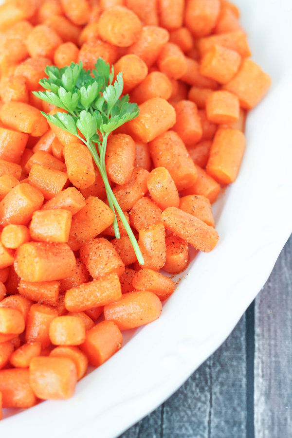 A large white casserole dish is full of roasted creole carrots. A sprig of parley is garnishing the top.