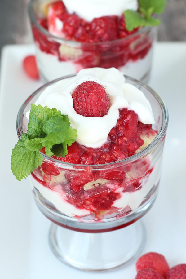 Two glass trifle bowls are full of chunks of pound cake and raspberry sauce. They have whipped cream on top for raspberry shortcake.