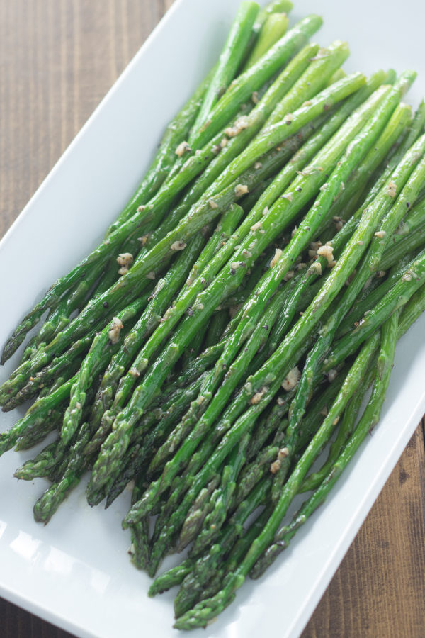 A white platter of tender spears of green asparagus sautéed in garlic butter.