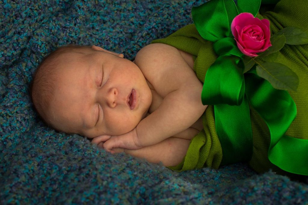 Ella on a blanket wrapped in a green scarf with a green bow and pink rose.