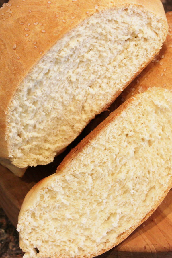 A large round loaf of bread baked in a cast iron skillet is sliced open showing the chew of the bread.