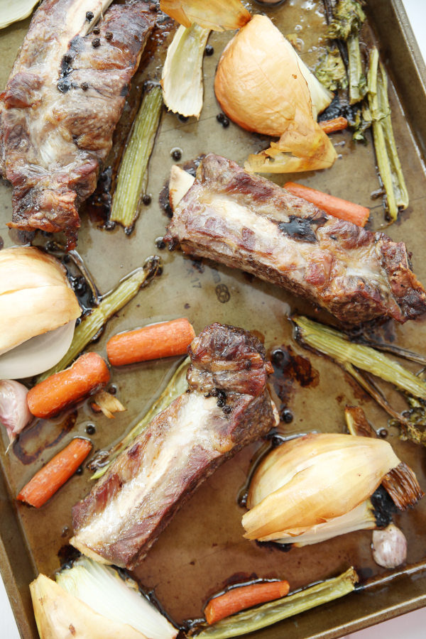 Roasted beef rib bones and vegetables are beautiful golden brown after roasting on a baking sheet.
