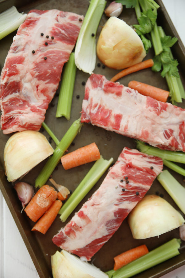 Beef rib bones, celery, onions and carrots are arranged on a baking tray before roasting for stock.