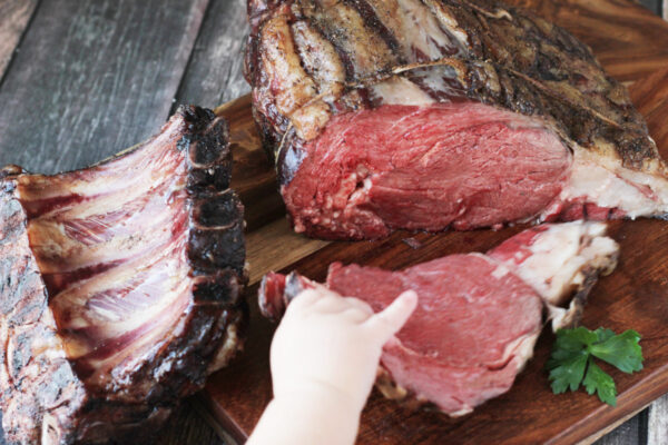 A little boy pulls a slice of prime rib off of the carving board.