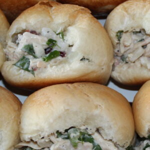 Fresh yeasty rolls are stuffed with classic chicken salad. You can see shredded chicken, sauce, celery, and other green herbs in the salad.