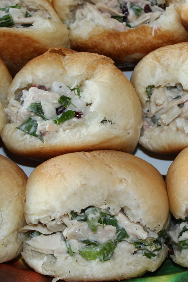 Fresh yeasty rolls are stuffed with classic chicken salad. You can see shredded chicken, sauce, celery, and other green herbs in the salad.