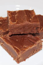 Four large squares of easy chocolate peanut butter fudge are stacked on a plate.