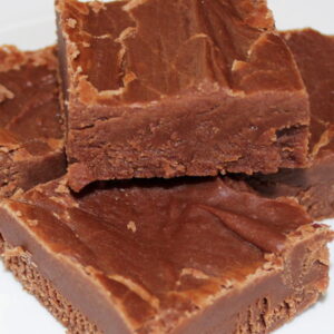 Four large squares of easy chocolate peanut butter fudge are stacked on a plate.