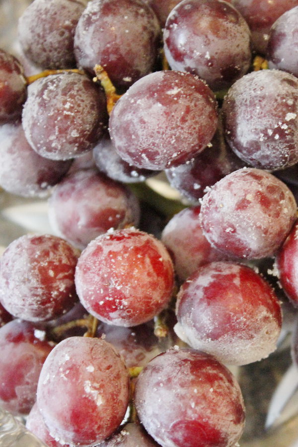 A pile of frozen red grapes sits on a plate. You can see the frosted look of the frozen grapes on the stem.