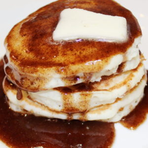 A stack of pancakes is covered with sticky bun pancake syrup with a pat of butter on the top.