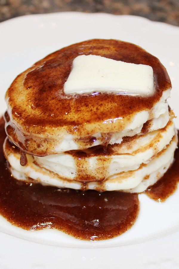 A stack of pancakes is covered with sticky bun pancake syrup with a pat of butter on the top.