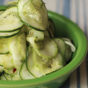 A green bowl is filled with fresh sliced cucumber dill salad. The cucumbers are piled high in the bowl.