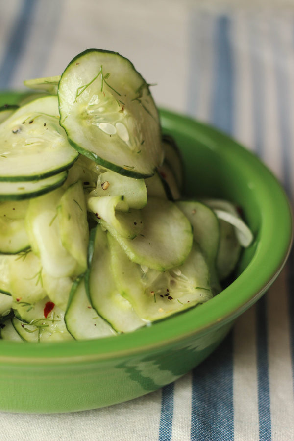 A green bowl is filled with fresh sliced cucumber dill salad. The cucumbers are piled high in the bowl.