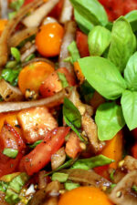 tomato salad with a big sprig of basil. This is a close up photo that shows cut tomatoes, torn basil and onions in a balsamic dressing