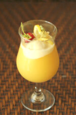 A tropical cocktail glass is full of a pineapple vodka cocktail based on the Dole Whip flavor. There is a scoop of ice cream, a strawberry and some lemon slices as garnish.