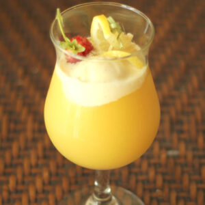 A tropical cocktail glass is full of a pineapple vodka cocktail based on the Dole Whip flavor. There is a scoop of ice cream, a strawberry and some lemon slices as garnish.
