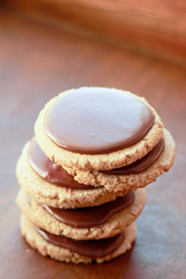 A stack of soft, chewy peanut butter cookies sits on a tray. Each cookie has a layer of rich chocolate frosting poured on.
