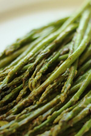 Asparagus that has been roasted in miso paste is lying on a white platter ready to serve for dinner.