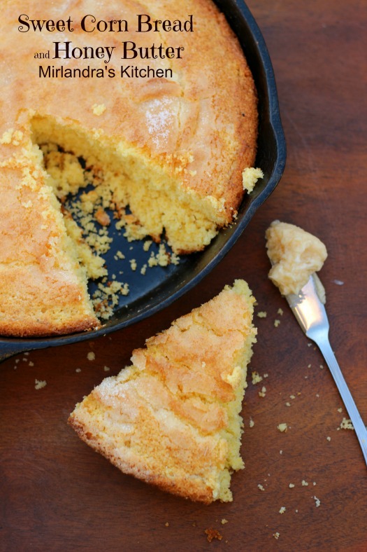 Golden corn bread with a sugar crust is baked in a cast iron skillet. There is a wedge sitting on the table next to a dollop of butter ready to spread.