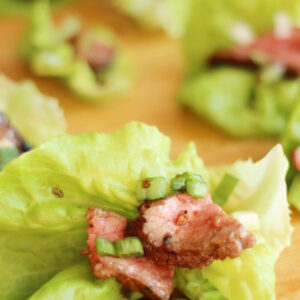 Korean BBQ beef slices sit on a lettuce leaf. There is a garnish of green onions and drizzle of sauce.