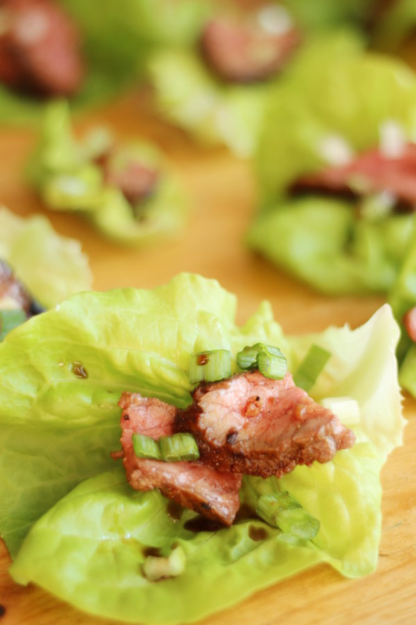 Korean BBQ beef slices sit on a lettuce leaf. There is a garnish of green onions and drizzle of sauce.