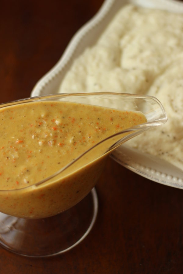 A gravy boat full of roasted vegetable turkey gravy sits ready to be used in on the mashed potatoes next to it.