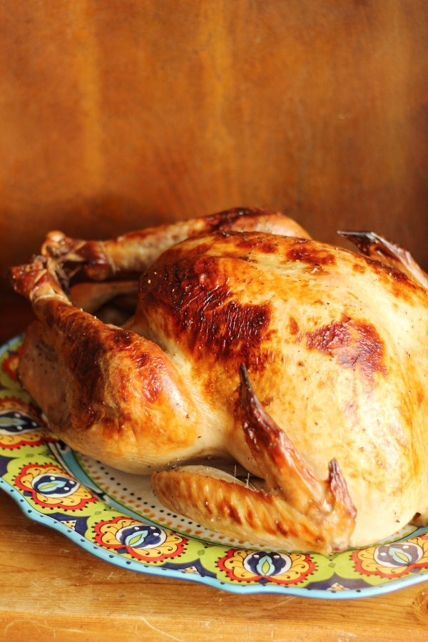 A beautiful brined and roasted turkey sits on a Spanish platter ready to be enjoyed. The platter is on a wooden table.