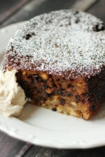 A Christmas pudding sits on a white plate. The front has been sliced off and you can see a bit of hard sauce next to it.