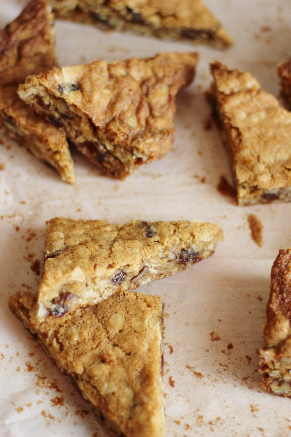 Oatmeal raisin cookie bars are cut into triangles and scattered on parchment paper.