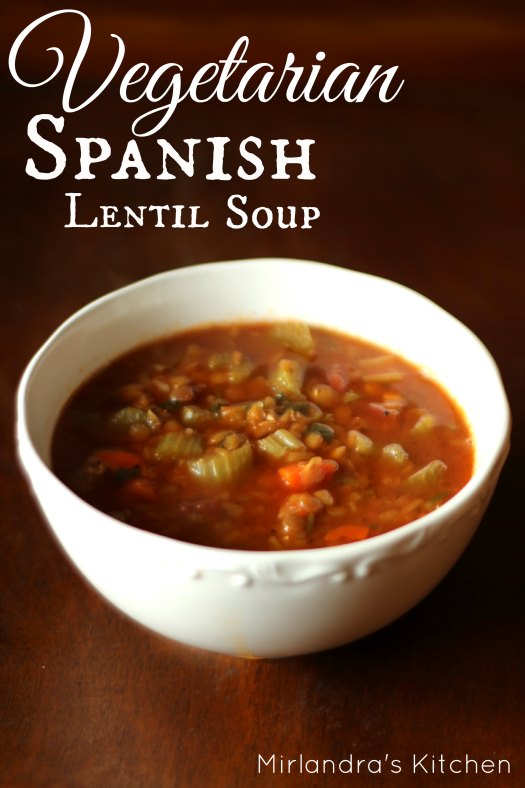 A big bowl of Spanish lentil soup sits on a wooden table. You can see celery, carrots and lentils in the soup.