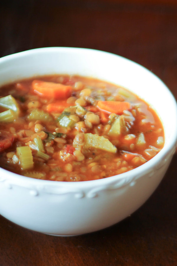 A large white bowl of Spanish lentil soup. You can see celery, carrots and lentils in a savory red broth.