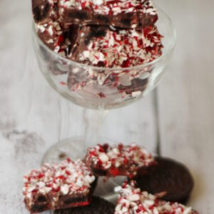 A stemmed glass is full of pieces of peppermint Oreo bark. There are additional pieces on the table with Oreo cookies.