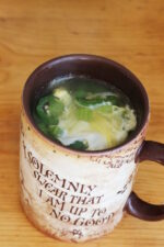 Large mug on a table full of soup. You can see a slice of jalapeno, the cooked egg, and a nice broth in the soup.