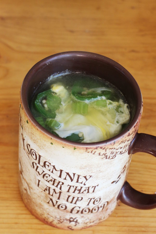 Large mug on a table full of soup. You can see a slice of jalapeno, the cooked egg, and a nice broth in the soup.