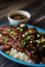 Blue platter of rice heaped up with Korean BBQ Ribs and garnished with green onions. Dipping sauce in the background.