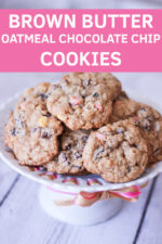 A white pedestal dish holds brown butter oatmeal chocolate chip cookies ready to serve. The dish has some ribbons wound through holes in the rim.