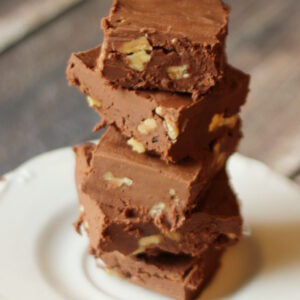A stack of squares of no cook fudge with walnuts is resting on a white plate.