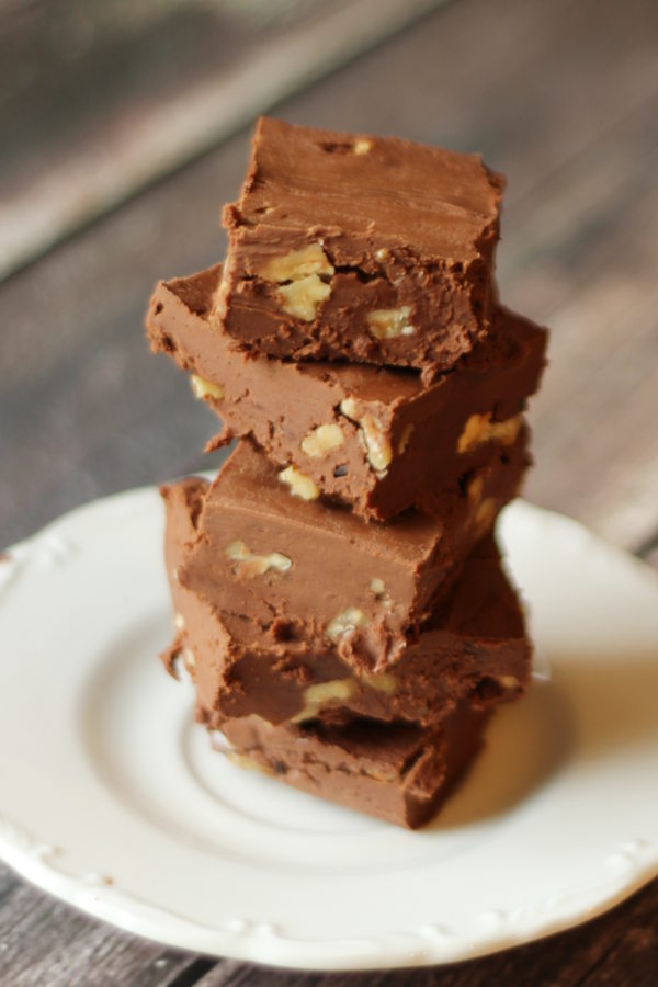 A stack of squares of no cook fudge with walnuts is resting on a white plate.