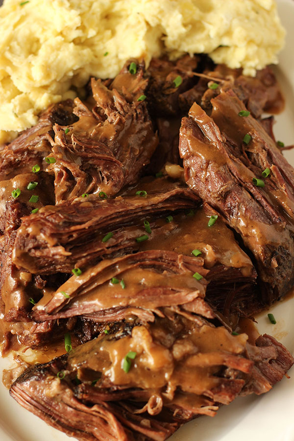 This slow cooker pot roast is piled high on a platter, drizzled with brown gravy and served with a fluffy pile of Yukon gold mashed potatoes.
