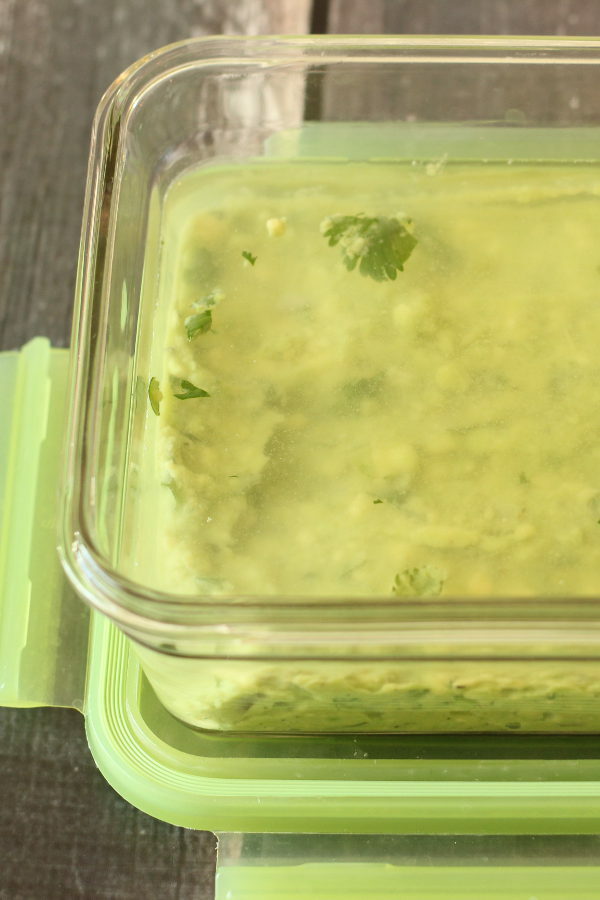 A glass container is full of guacamole. There is a layer of water on top to keep it from browning.