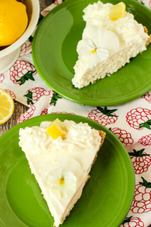 Two slices of lemonade icebox pie sit on green plates. They are garnished with a pansy and slice of lemon.
