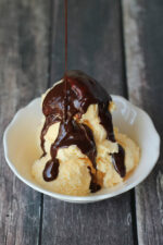 decadent hot fudge sauce is drizzled over vanilla ice cream in a white bowl.