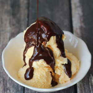 decadent hot fudge sauce is drizzled over vanilla ice cream in a white bowl.