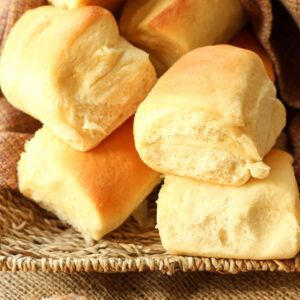 A basket is loaded up with big golden copycat Texas Roadhouse Rolls. Next to the rolls is a dish of cinnamon honey butter.